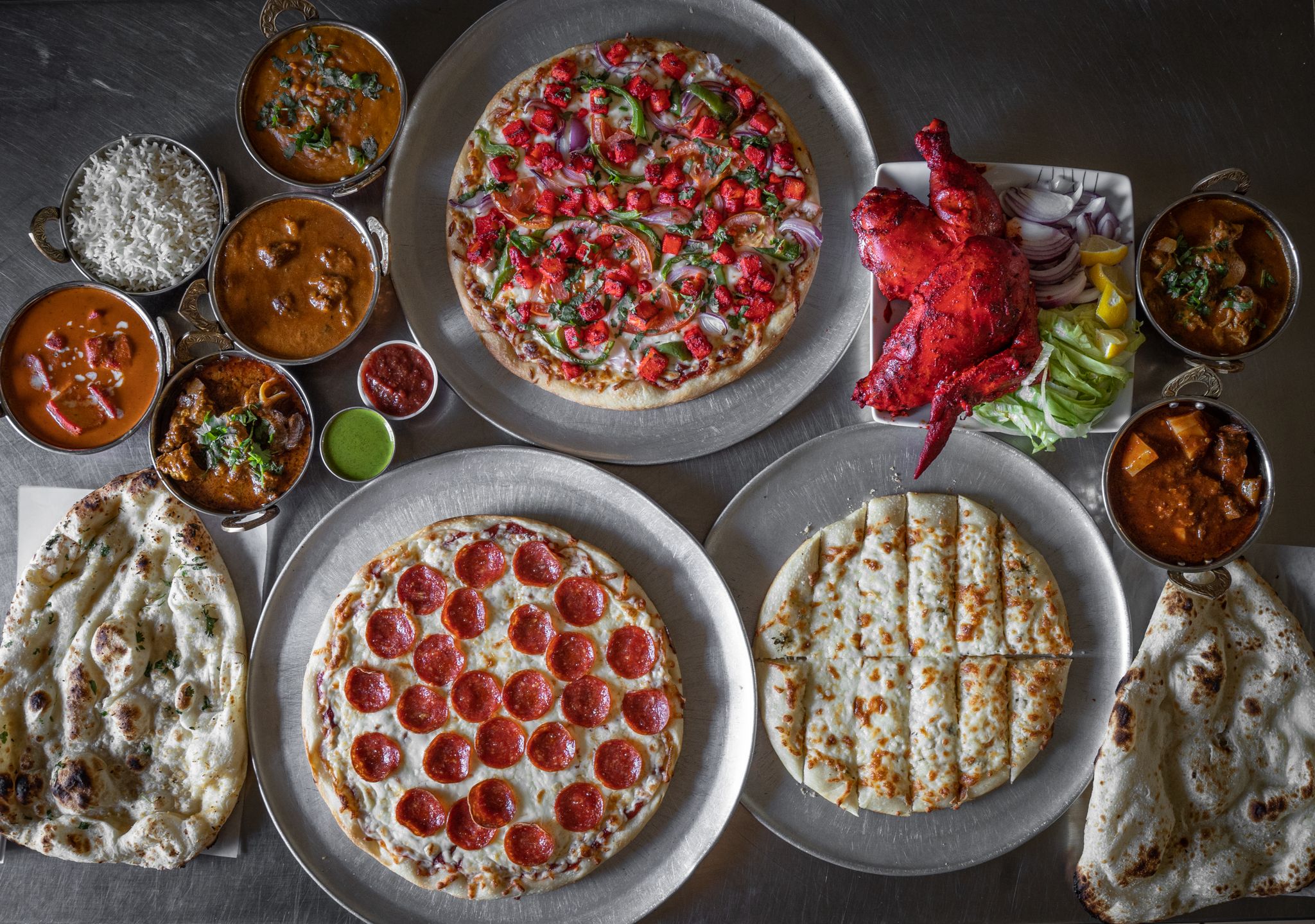 A diverse selection of Indian curries and Italian pizzas in a vibrant flat lay setting.