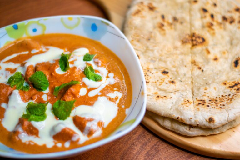 Close-up of flavorful butter chicken with naan bread, garnished with mint leaves.