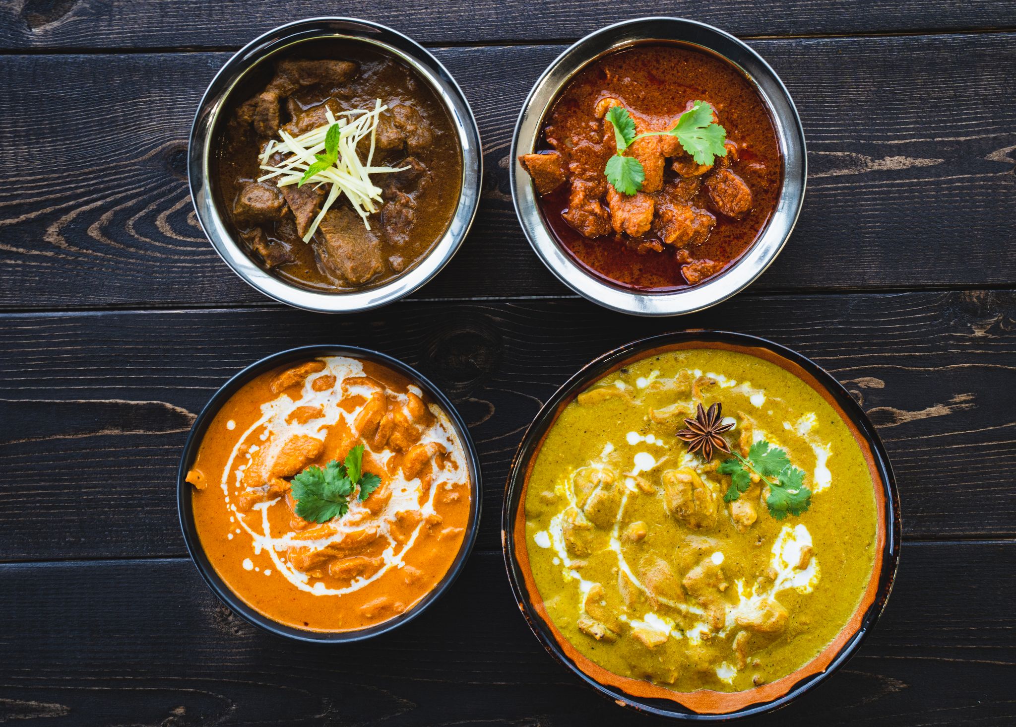 Vibrant Indian curries in bowls on a dark rustic table, ideal for food enthusiasts.